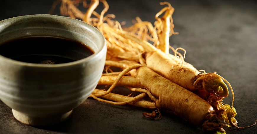 tasse fumante de tisane de ginseng rouge en poudre avec racines séchées de panax ginseng disposées à côté sur table en bois rustique avec cuillère de miel
